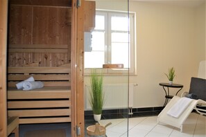 Un sauna en bois avec des bancs, une petite table ornée d’une plante et une chaise avec une serviette.