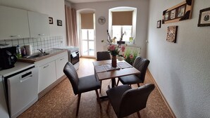 A compact kitchen with white cabinets, a dining table with four chairs, and a vase with flowers.