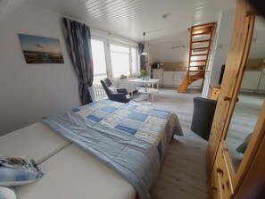 Quarto com cama, escrivaninha, cadeira e vista para cozinha e varanda.