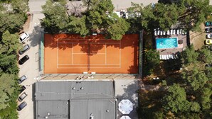 An aerial view of a tennis court surrounded by trees, with a pool and lounge chairs on one side. - Morski Park Międzywodzie (Dziwnów)