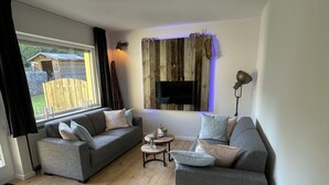 A modern living room with two grey sofas, a small round table, and a TV mounted on a wooden wall. - Your own home in the Sauerland, relax if you can! (Willingen)