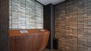 A reception area with a wooden counter and a tiled wall. - GRAND BASE Saiwaimachi (Nagasaki)