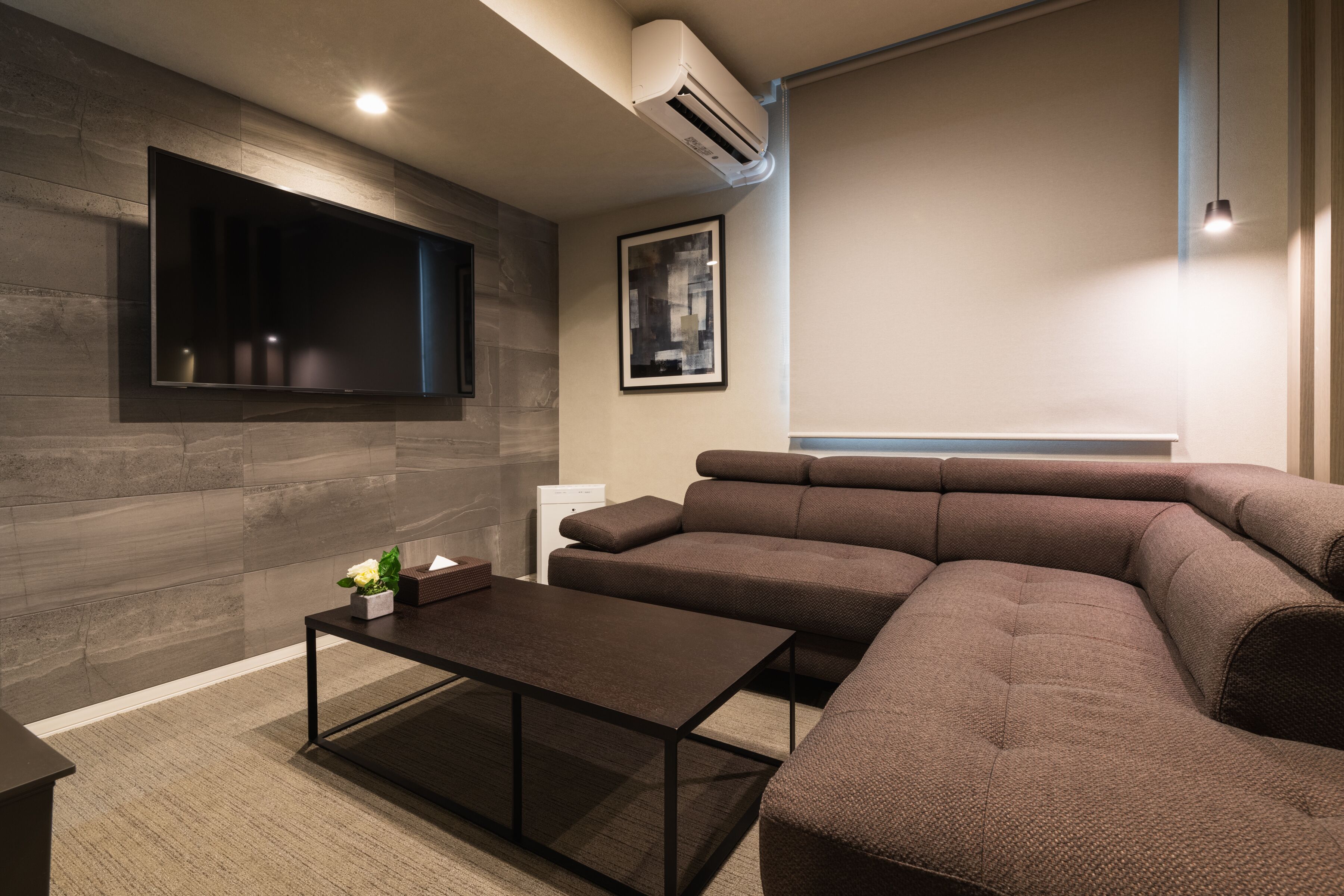 Un salon moderne avec un canapé d’angle, un téléviseur à écran plat fixé au mur, une table basse et un tableau encadré.