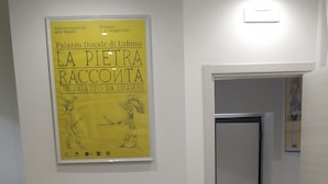 Un coin repas avec une table ronde et quatre chaises blanches aux pieds en bois. Une affiche jaune, ornée d’un texte et d’un dessin, est accrochée au mur au-dessus de la table.