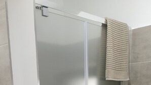 Une cabine de douche fermée par des parois en verre, avec une serviette accrochée à la porte.
