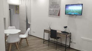 Une chambre moderne équipée d’un bureau, d’une chaise et d’un téléviseur diffusant un match de football.