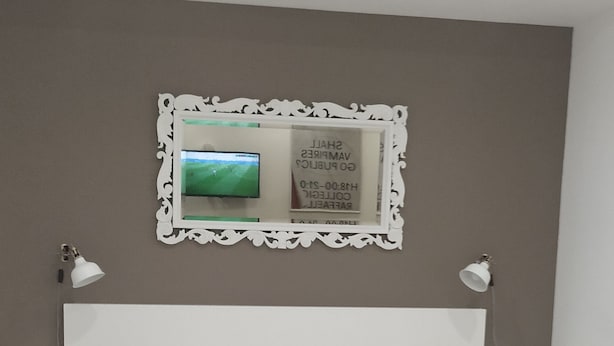 Une chambre à coucher bien rangée, avec un lit, deux tables de chevet, un téléviseur fixé au mur et un panneau décoratif encadré.