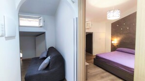A bedroom with a bed, a seating area with cushions, a wardrobe, and a small window. - Antica Assisi Apartment - in the Historic Center with Bedroom, Bath and Kitchen (Assisi)