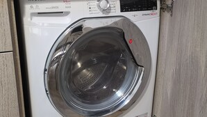 A white front-loading washing machine with a control panel, located in a wooden cabinet. - Antica Assisi Apartment - in the Historic Center with Bedroom, Bath and Kitchen (Assisi)