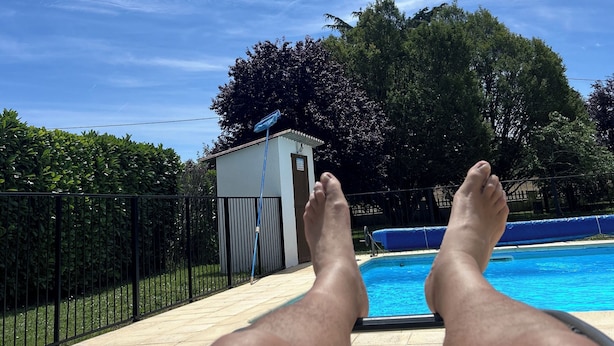 Vista a la piscina bajo un cielo despejado, con una piscina y un edificio pequeño al fondo.