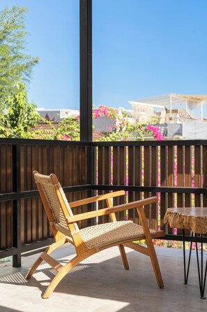 A wooden chair and table on a balcony with a view of pink flowers and a clear blue sky. - Villa Ziggy (Canggu)