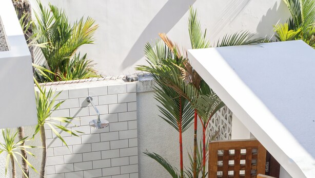 A small, enclosed outdoor shower area with a tiled wall, potted plants, and a wooden gate.
