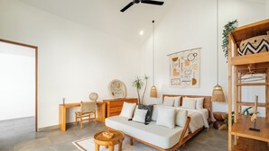 A modern bedroom with a bed, a sofa, a desk, and a hanging plant.