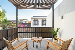 A covered balcony with two wicker chairs and a small round table, a potted plant, and a building with arched windows in the background. - Villa Ziggy (Canggu)
