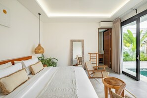 Habitación de hotel moderna con una cama grande, sillas de madera, una mesita, una lámpara colgante, un espejo y vistas a una piscina.