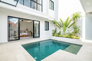 Une maison moderne dotée d’une piscine, d’une entrée avec une porte en verre et d’un patio agrémenté de plantes.