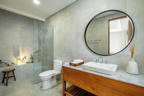 A modern bathroom with a glass-enclosed shower, a toilet, a vanity with a sink, and a round mirror.