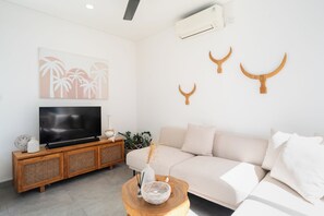 A modern living room with a flat-screen TV, a wooden console, a beige sofa, and decorative wall art. - Villa Ziggy (Canggu)