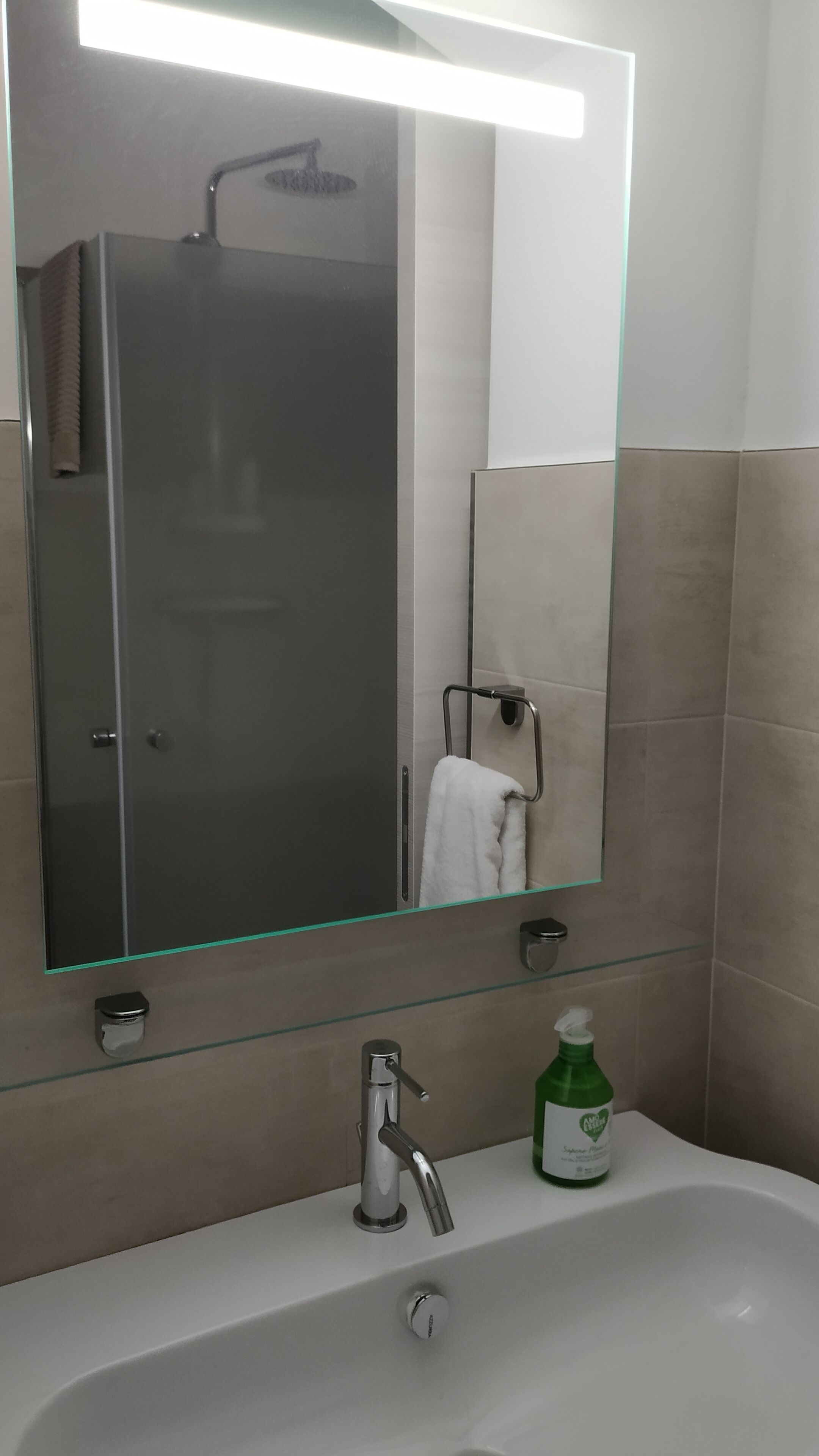 Une salle de bain avec une douche à parois de verre, un lavabo blanc avec une bouteille verte et un porte-serviettes.