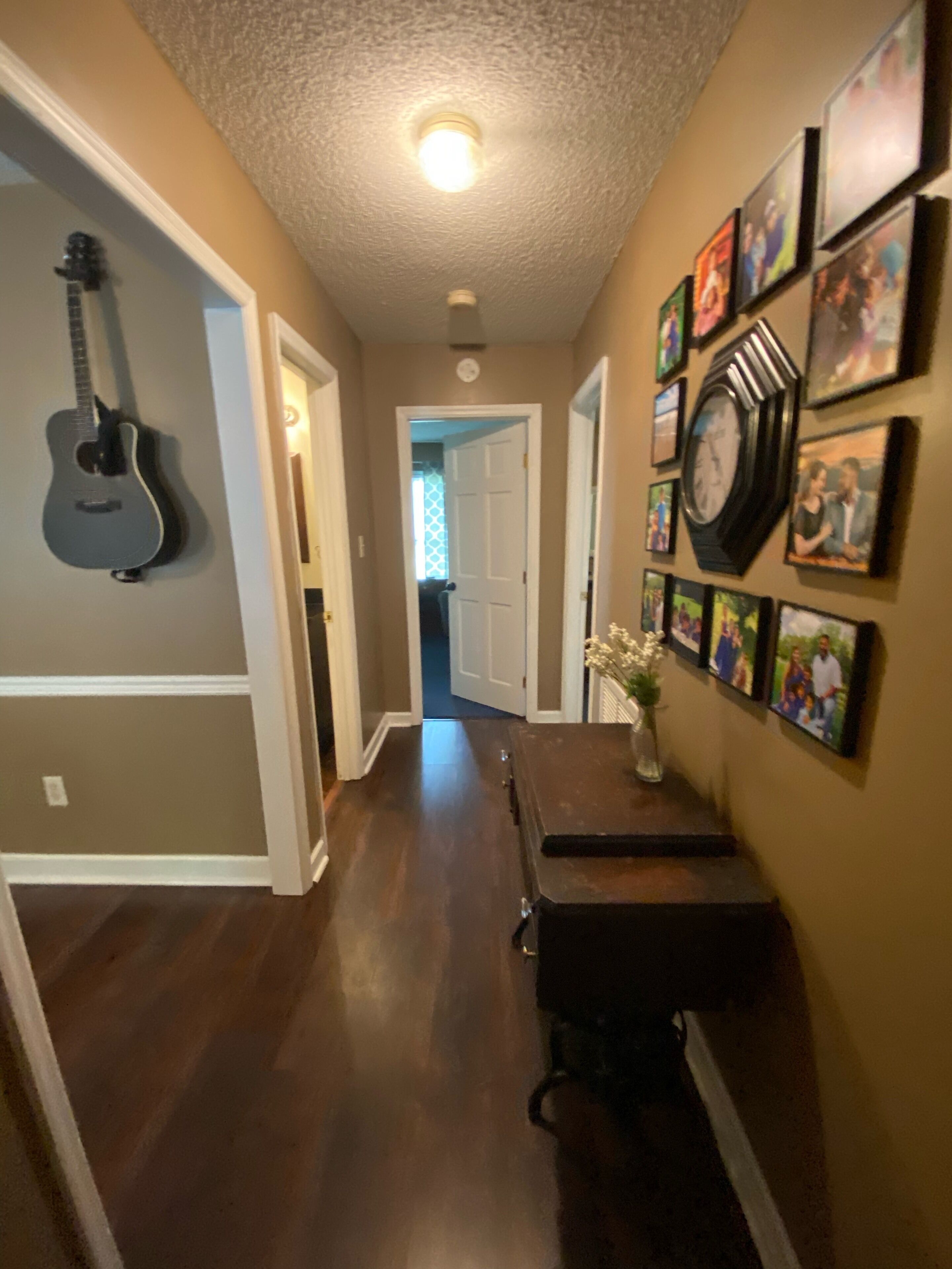 A hallway with a guitar, a clock, and framed photos on the walls.