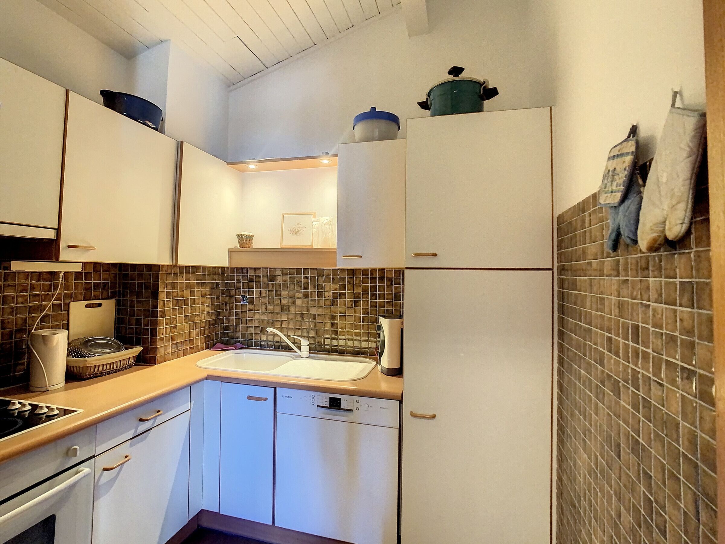 Een compacte keuken met witte kasten, een betegelde spatwand, een gootsteen en een fornuis.