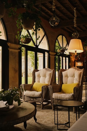 A room with arched windows, wicker furniture, and hanging plants. - Helguera Palacio Boutique & Antique (Puente Viesgo)