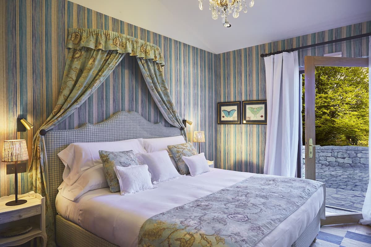 A bedroom with a large bed, striped wallpaper, and a view of greenery outside.
