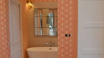 Un baño con una bañera independiente, un espejo sobre el lavabo y un papel pintado estampado.