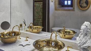A bathroom with a large mirror, two gold sinks, a white towel, and a statue.
