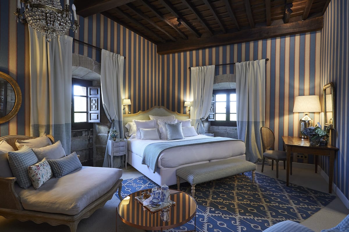 A hotel room with a large bed, a sofa, a round coffee table, and a desk with a lamp.