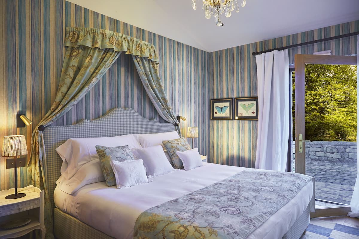 A bedroom with a bed, curtains, a chandelier, and a view through an open door.