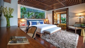 Een moderne hotelkamer met een groot bed, een houten bureau, een comfortabele fauteuil en uitzicht op groen door het raam.