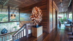 Een houten interieur met een trap, een groot abstracte sculptuur en uitzicht op groen.