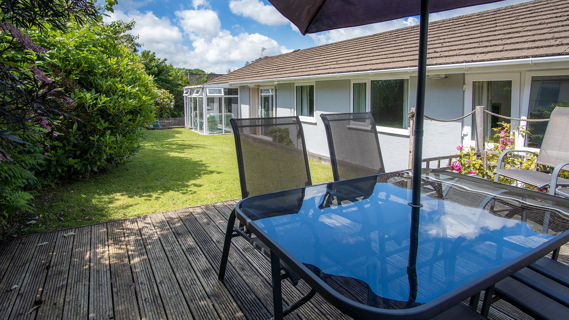 A patio with a glass table and chairs, a wooden deck, and a conservatory.