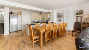 A modern kitchen with wooden cabinets, a dining table with chairs, and a leather sofa in a bright room with white walls and wooden flooring. - Kilmore - Beach Front House Direct Beach Access Spectacular Sea Views (Saundersfoot)