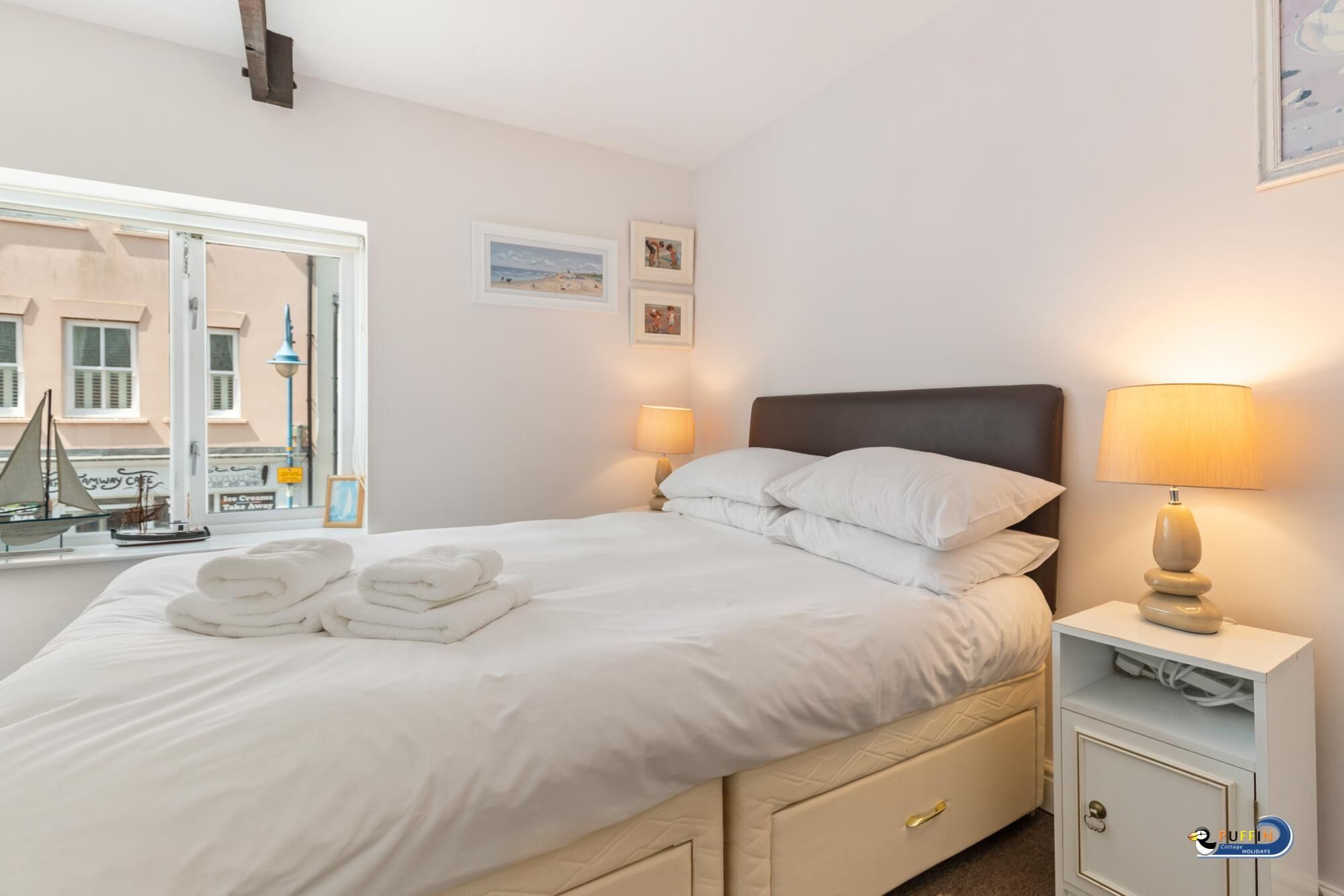 A neatly made bed with white linens and towels, a bedside table with a lamp, and a small cabinet.