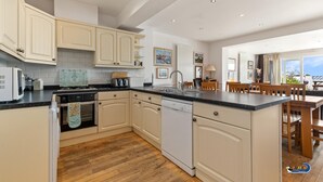 A spacious kitchen with white cabinetry, a central island, and a view to the dining area. - Kilmore - Beach Front House Direct Beach Access Spectacular Sea Views (Saundersfoot)