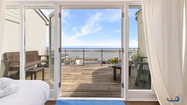 A bedroom with a large sliding glass door leading to a wooden deck overlooking a beach. - Kilmore - Beach Front House Direct Beach Access Spectacular Sea Views (Saundersfoot)