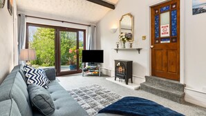 A living room with a sofa, a TV, a fireplace, and a door with a 'Private' sign. - The Hollies - Short Walk to Beach Peaceful Location Parking (Narberth)