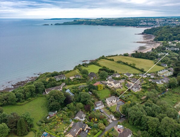 An aerial view of The Hollies, a residential area with houses, green spaces, and a coastline.