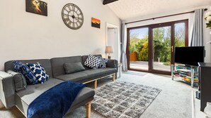 A modern living room with a grey sofa, decorative pillows, a blue throw blanket, a large clock, and a bookshelf with books. - The Hollies - Short Walk to Beach Peaceful Location Parking (Narberth)