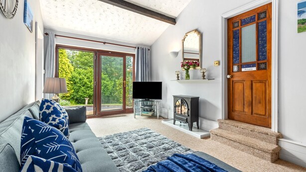 A living room with a sofa, TV, fireplace, and a large sliding glass door leading to a garden. - The Hollies - Short Walk to Beach Peaceful Location Parking (Narberth)