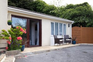 A single-story house with a sliding glass door entrance, a small patio with outdoor furniture, and a wooden fence in the background.