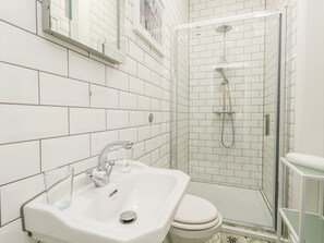 A modern bathroom with white tiles, a sink, a toilet, and a glass-enclosed shower area. - The Kings Vista (Weymouth)