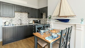 A modern kitchen with dark cabinets, a tiled backsplash, and a wooden dining table set for two. - The Kings Vista (Weymouth)