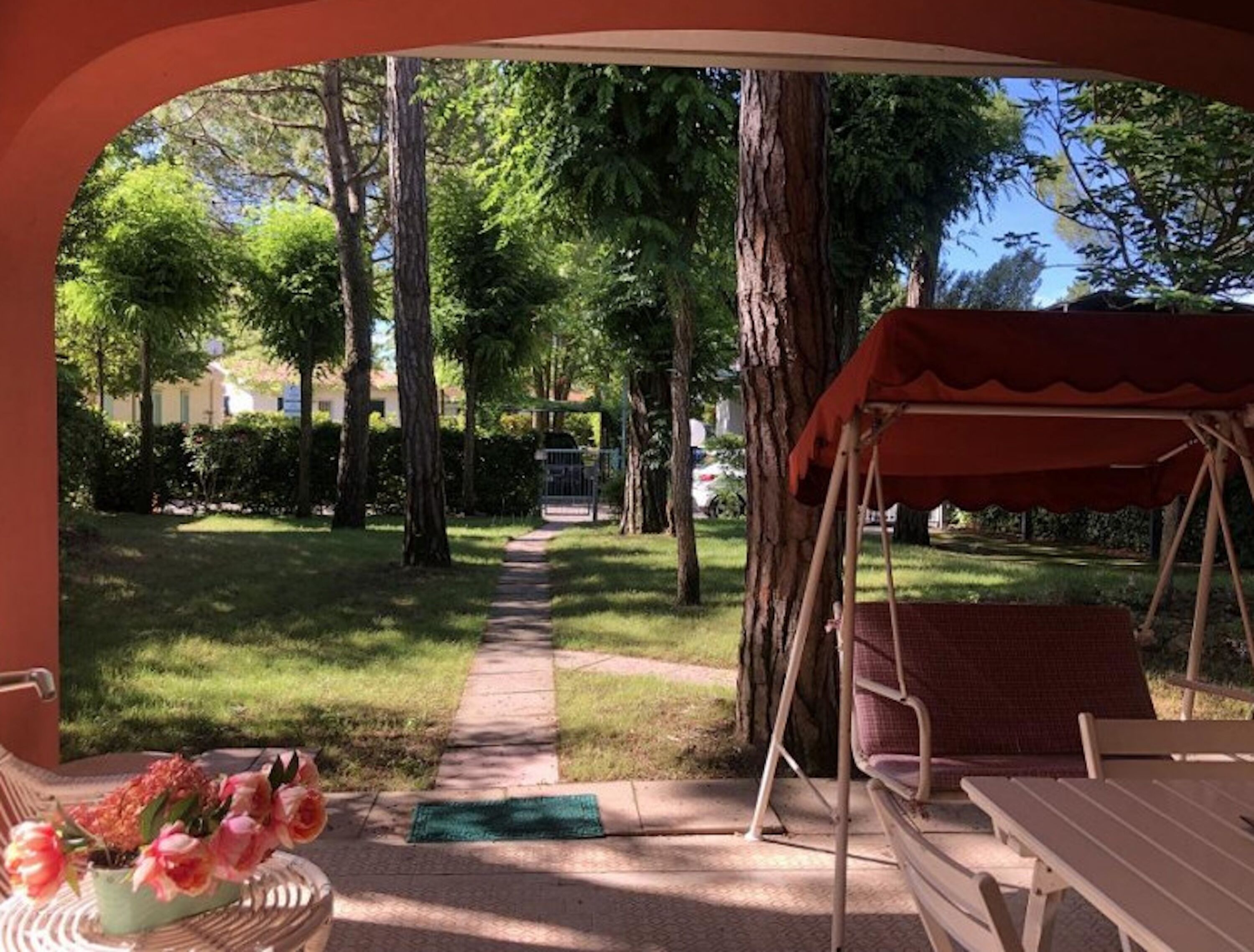 A patio area with a swing set, a table, and a chair. There is a pathway leading to a gate.