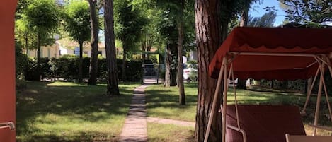 A patio area with a swing set, a table, and a chair. There is a pathway leading to a gate.