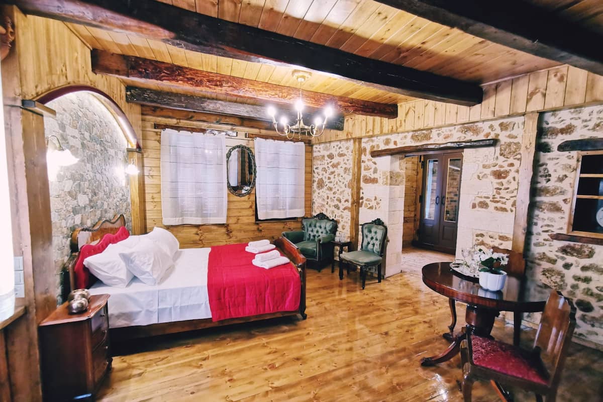 Een slaapkamer met houten vloer, een bed, twee stoelen, een tafel en een spiegel.