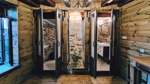Een houten blokhut interieur met een centrale stenen muur, houten vloeren en een kroonluchter.