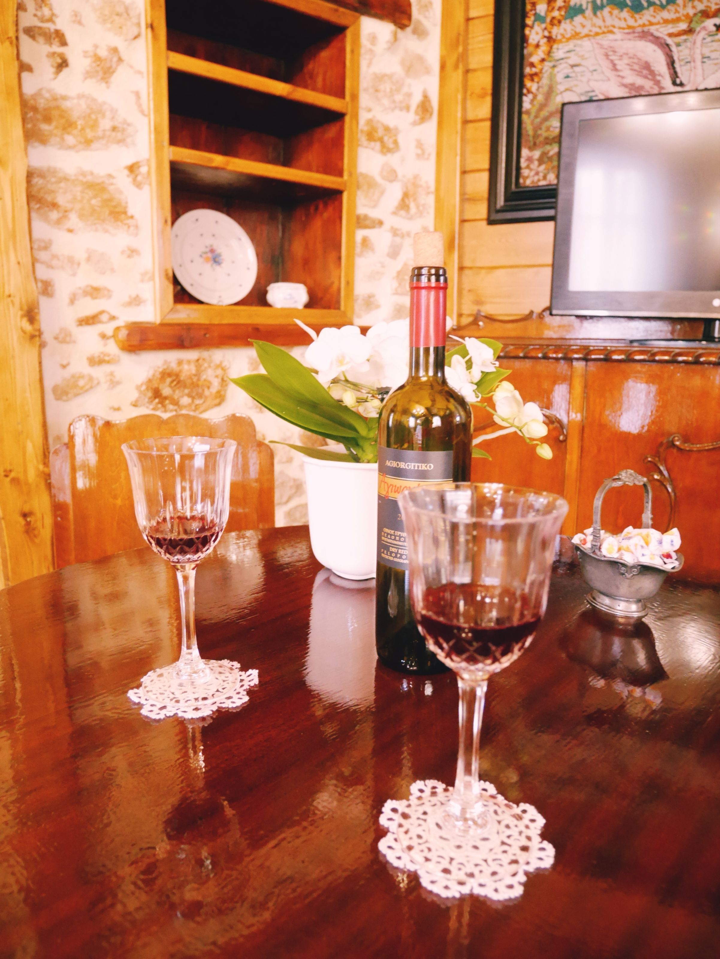 Una mesa de madera con dos copas de vino, una botella y un recipiente pequeño con aperitivos.